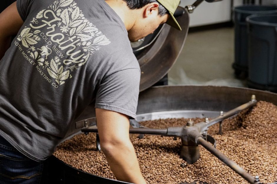 view of coffee roaster from behind with their hands in freshly roaster coffee beans.